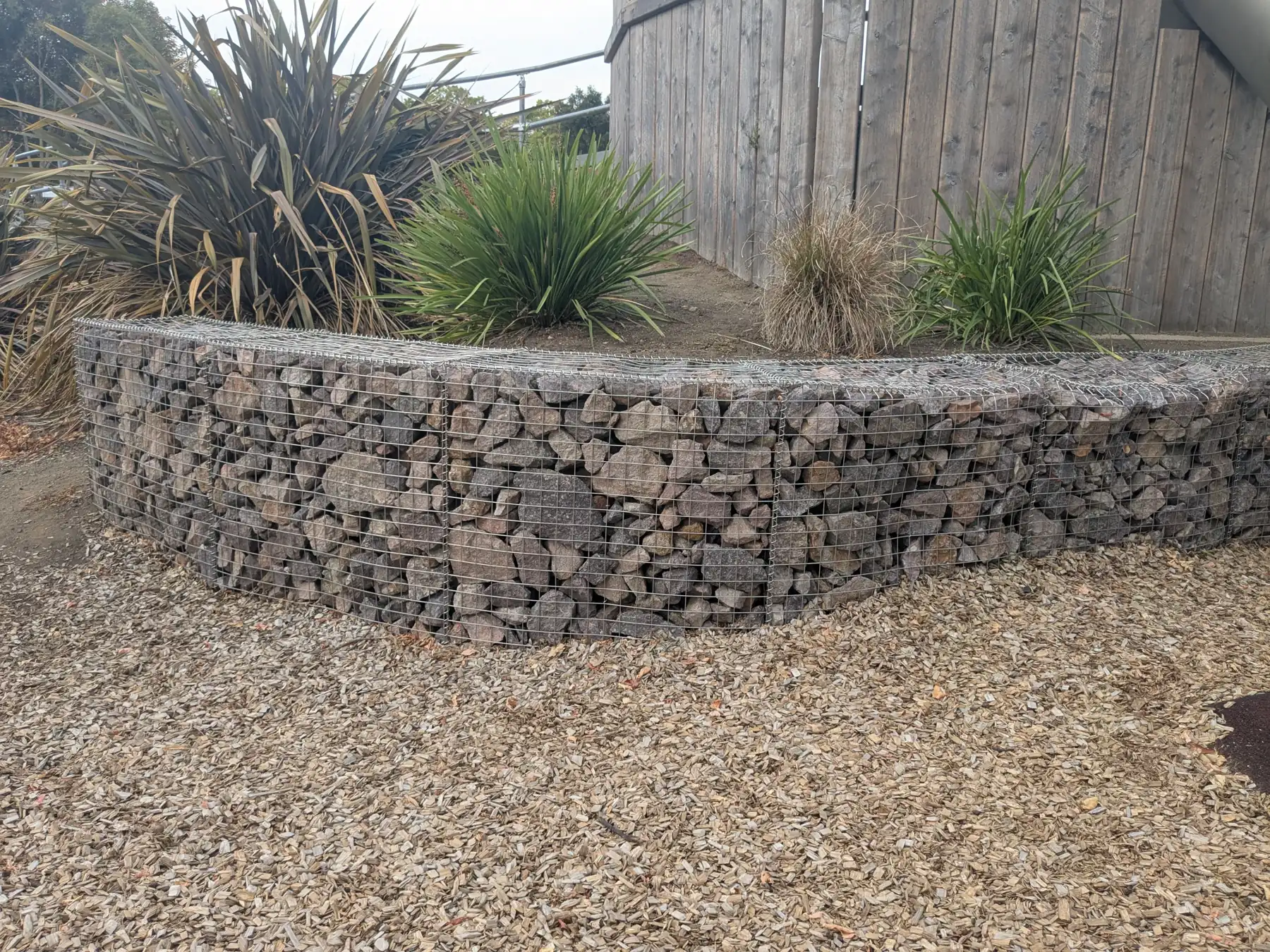 Curved gabion retaining wall of rock-filled wire cages beside a gravel path